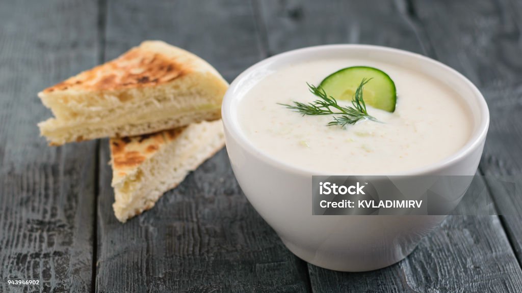 Freshly made tzatziki in a white bowl with bread on a dark wooden table. Freshly made tzatziki in a white bowl on a dark wooden table. Vegetarian Greek cuisine. Appetizer Stock Photo