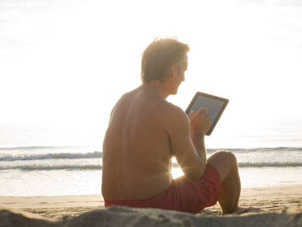 istock Man reads from tablet computer on lounge chair at waters edge 943974486