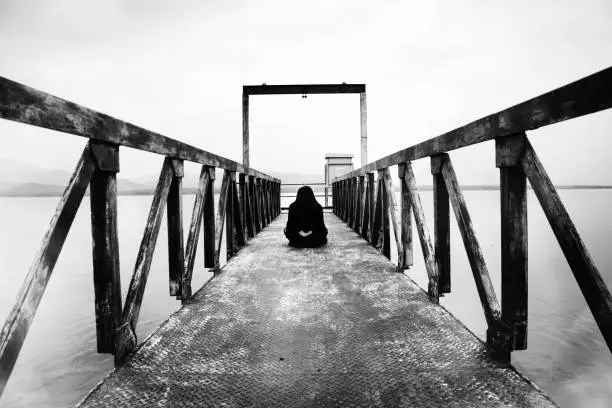 Photo of woman sitting at water level gate, horror scene in white tone