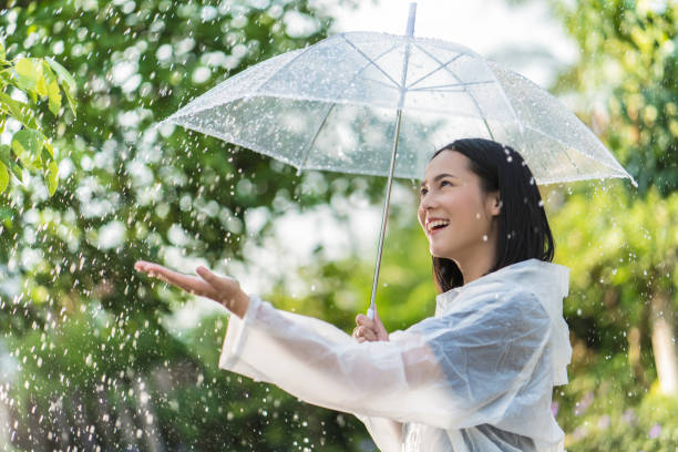 アウトドア レインコートを着て雨の日のアジア女性。彼女は幸せです。彼女は雨に触れる彼女の手を使用します。 - umbrella women storm yellow ストックフォトと画像