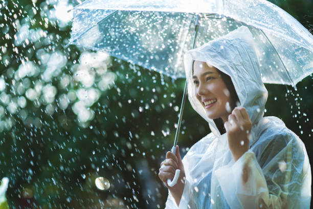 アウトドア レインコートを着て雨の日のアジア女性。彼女は幸せです。 - umbrella women storm yellow ストックフォトと画像