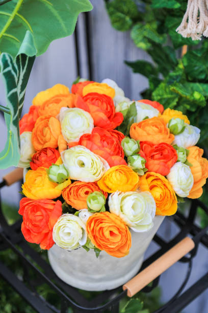 istock A colorful artificial flowers in a white pot on black metal shelf with nature background. 943977708