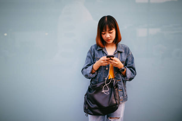 istock Young Asian woman in Bangkok downtown district, taking a break, texting on the cell while having a drink 943985678