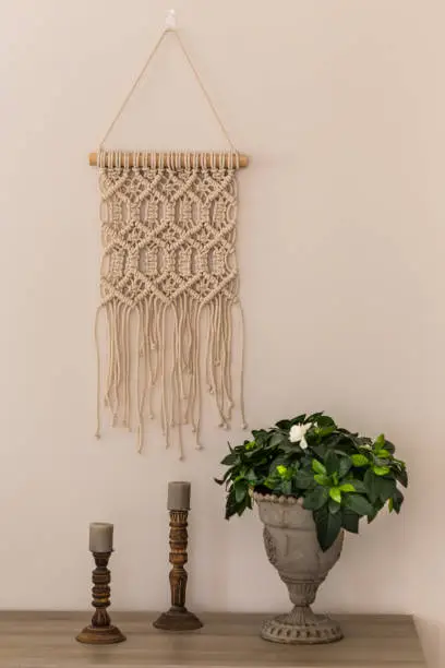 Interior decoration concept. Macrame wall art, wooden candleholders and gardenia flower in metal vase. Vertical composition.