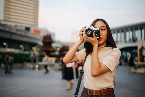 Young Asian woman traveler in Bangkok downtown district, holding a vintage film camera