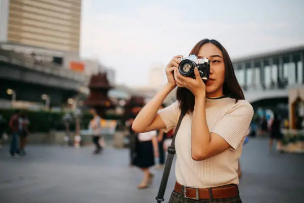 Photo of Young Asian woman traveler in Bangkok downtown district, holding a vintage film camera