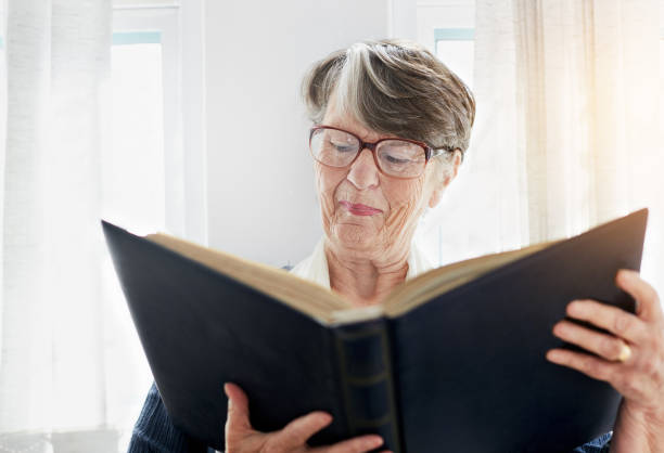 istock Old woman looking at book smiles, remembering 943999454