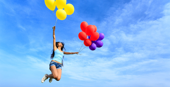 Cheerful young woman holding multicolored balloons jumping