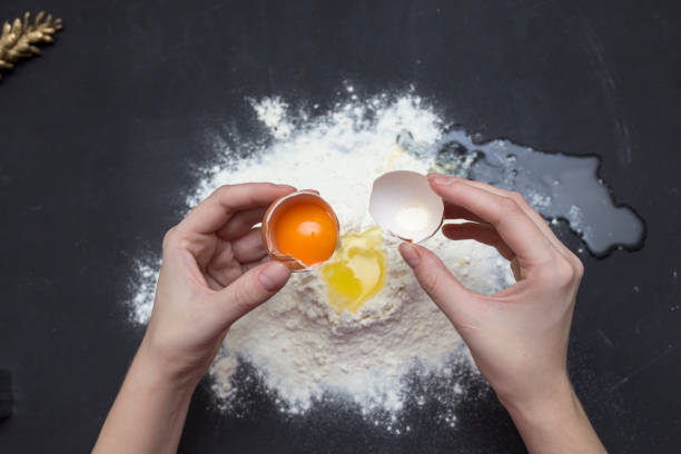 istock Chicken eggs in white plate and slide around her meal with a broken egg. The process of making of the test. Eggs, flour, a plate on a black background. 944004550