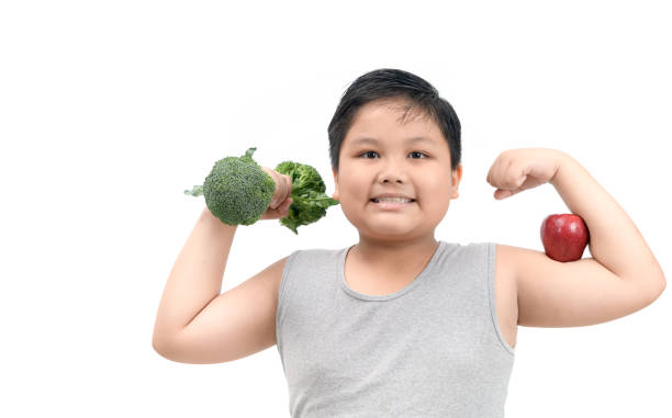 Obese fat boy holding a broccoli dumbbell Obese fat boy holding a broccoli dumbbell and show muscle with apple isolated on white background, diet and exercise for good health concept overweight child stock pictures, royalty-free photos & images