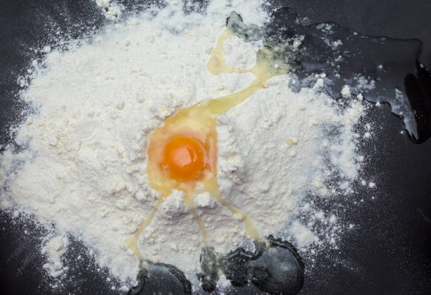 istock Chicken eggs in white plate and slide around her meal with a broken egg. The process of making of the test. Eggs, flour, a plate on a black background. 944004718
