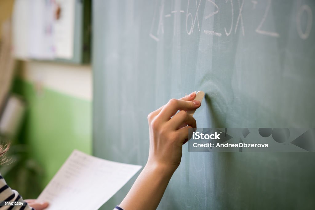 Young female teacher or a student writing math formula on blackboard in classroom. Teacher Stock Photo