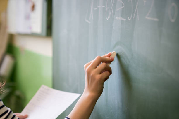 Young female teacher or a student writing math formula on blackboard in classroom. stock photo