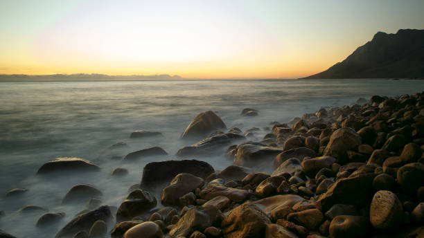 A beautiful long exposure seascape at sunset with rocks and moving water and a mountain at Kogel Bay False Bay Cape Town Strand South Africa