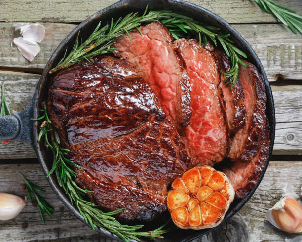 vue de dessus d’un boeuf steak saignant avec cuit l’ail et le romarin dans le plâtre noir pan au-dessus d’une table rustique. - close up roasted meal pepper photos et images de collection