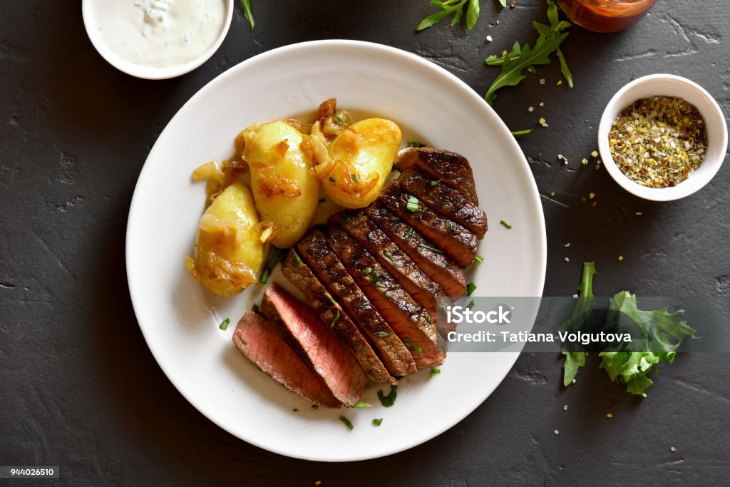 Beef steak with potato Tasty sliced medium rare roast beef with potato over black stone background. Top view, flat lay Plate Stock Photo