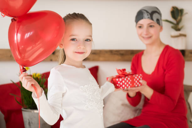 giovane madre, paziente oncologa e sua figlia carina, che festeggiano il ritorno a casa dall'ospedale. bentorna a casa o festa di compleanno con palloncini e regali. - cancer chemotherapy drug baby family foto e immagini stock