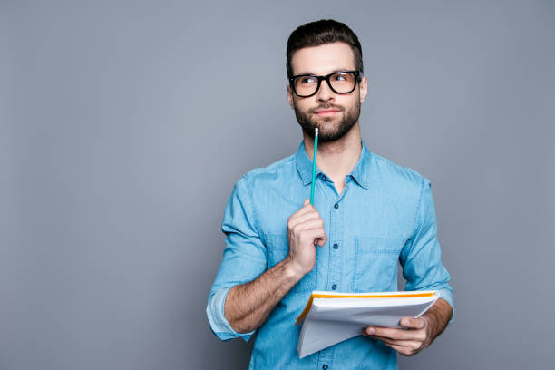 istock Young bearded guy in glasses holding a notebook and thinking about exams 944038866