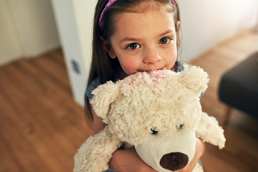 High angle portrait of an adorable little girl tightly hugging her teddy at home during the day
