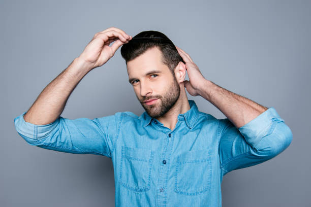 un ritratto di un bell'uomo sicuro di sé in camicia di jeans che si pettina i capelli - men hairdresser human hair hairstyle foto e immagini stock