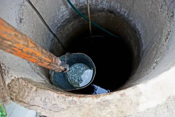 Photo of iron bucket with water at the depth of a round well