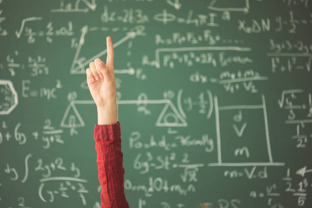 istock Student raised up hand pointing finger in front of green chalk board 944043452