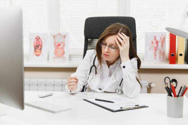 Female doctor sitting at desk with medical documents, clinical thermometer, high fever temperature in light office in hospital. Woman in medical gown, stethoscope in consulting room. Medicine concept. Female doctor sitting at desk with medical documents, clinical thermometer, high fever temperature in light office in hospital. Woman in medical gown, stethoscope in consulting room. Medicine concept niñas stock pictures, royalty-free photos & images