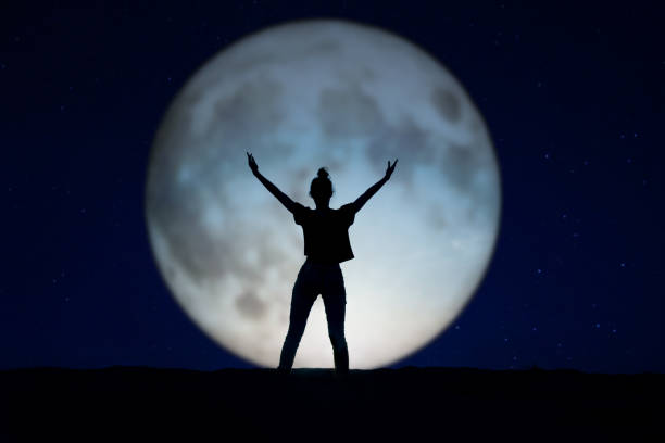 Silhouette of a woman standing in the night with the arms up, giant moon in the background Silhouette of a woman standing in the night with the arms up, giant moon in the background full moon photos stock pictures, royalty-free photos & images