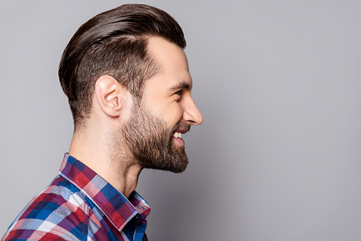 A side view portrait of young handsome smiling man with stylish haircut standing against gray background