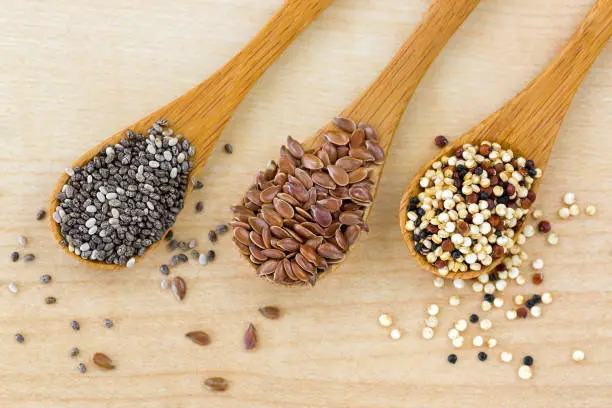 Dried Chia seed, Linseed flaxseed, Quinoa seed tri-color blend on wooden spoon, wood background