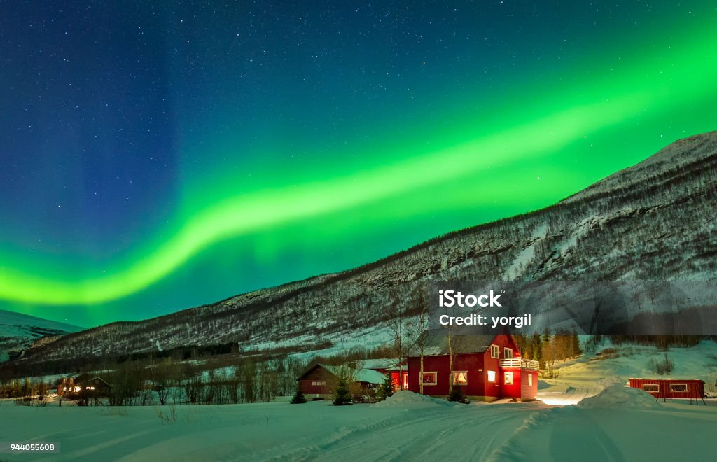 Northern lights over house at Norway countryside Aurora Borealis over mountain and rural house in distant Northern Norway. Green light of aurora lay over mountains. Tromso Stock Photo