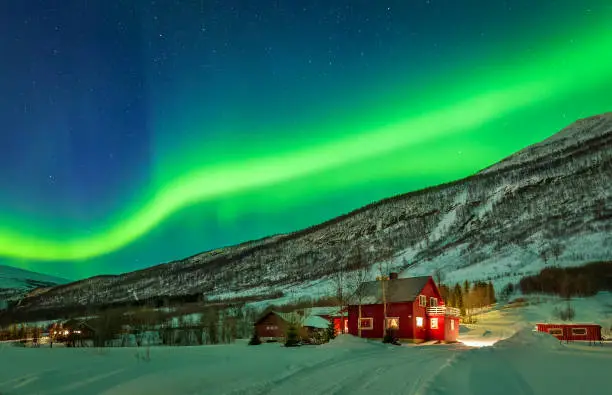 Aurora Borealis over mountain and rural house in distant Northern Norway. Green light of aurora lay over mountains.