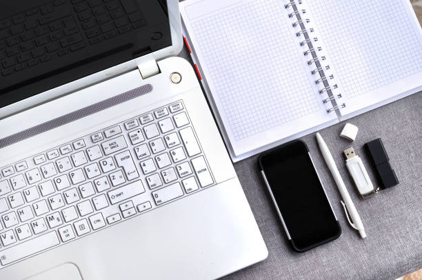 bem acima vista do escritório local de trabalho com telefone celular e laptop perto teclado de computador e mouse com caderno, caneta e usb flash na mesa cinza. conceito de mesa de mesa de blogging de trabalho - mobile office flash - fotografias e filmes do acervo