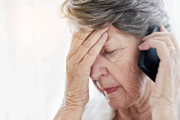 istock Old woman holding mobile phone closes eyes, looking distraught 944065126