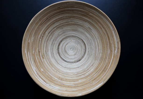Original wooden plate with continuous lines on the black table. Organic, natural material of bowl with eternal lines. Eco-friendly photo.