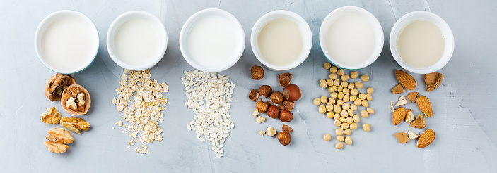 Food and drink, health care, diet and nutrition concept. Assortment of organic vegan non diary milk from nuts, oatmeal, rice, soy in glasses on a kitchen table. Top view flat lay background