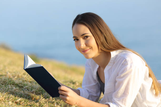 istock Woman reading a book looking at camera on the grass 944069576