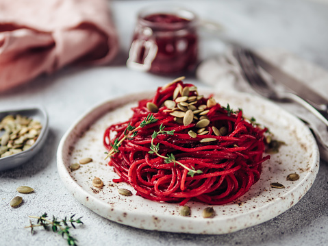 Roasted beetroot and thyme spaghetti with pumpkin seed in craft plate on gray cement background. Ideas and recipes for healthy vegan vegetarian dinner. Selective focus.