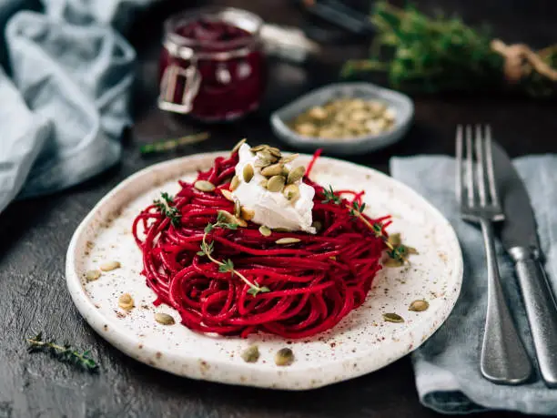 Roasted beetroot and thyme spaghetti with pumpkin seed in craft plate on dark tabletop. Ideas and recipes for healthy vegan vegetarian dinner. Selective focus.