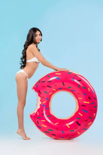 Photo of attractive girl posing with inflatable donut ring, isolated on blue