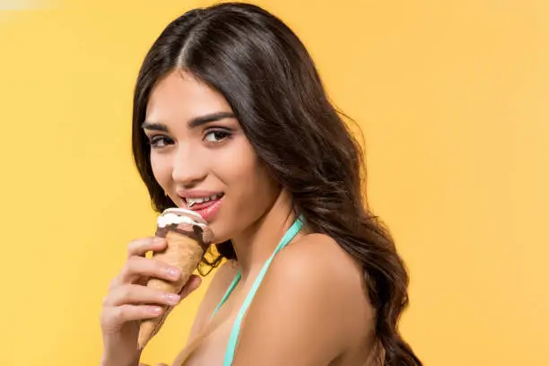 Photo of attractive girl eating ice cream cone, isolated on yellow