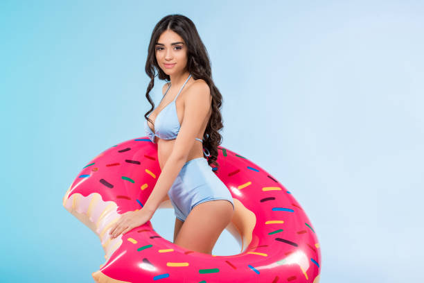 istock attractive brunette girl posing with inflatable donut ring, isolated on blue 944076516