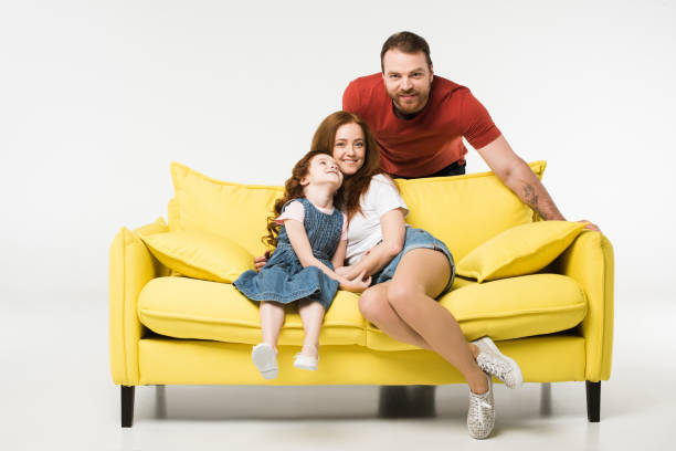 istock Mother and daughter on sofa while father standing behind isolated on white 944082094
