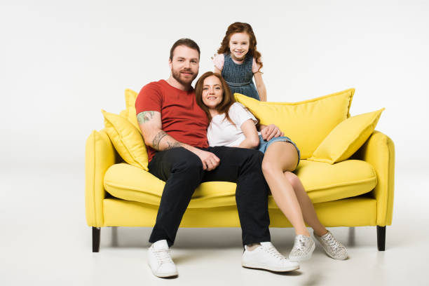 istock Couple sitting on couch with daughter behind isolated on white 944092916