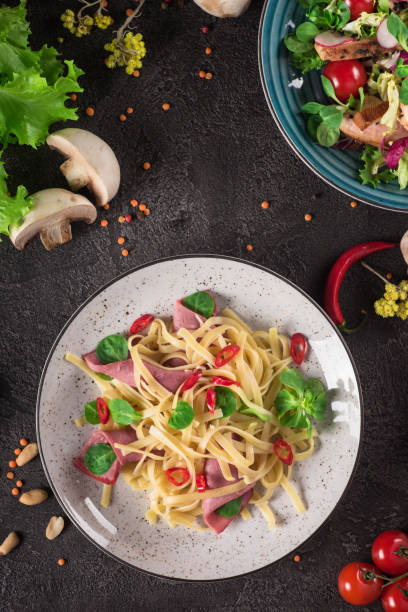 istock Italian spaghetti. Tagliatelle pasta with ham. Selective focus. Black background. Top view 944097042