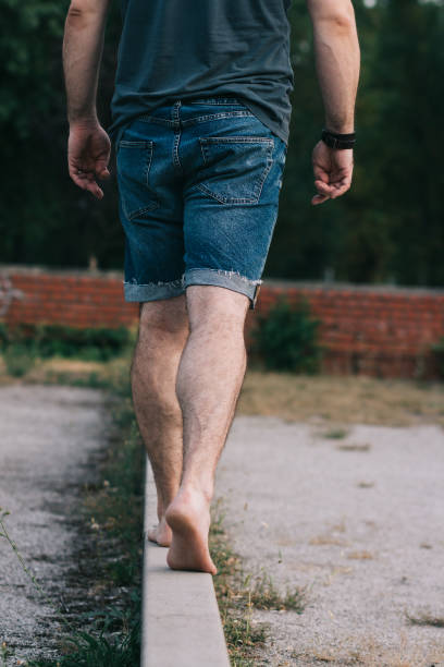 istock Barefoot man in jean shorts walking on narrow wall 944097356