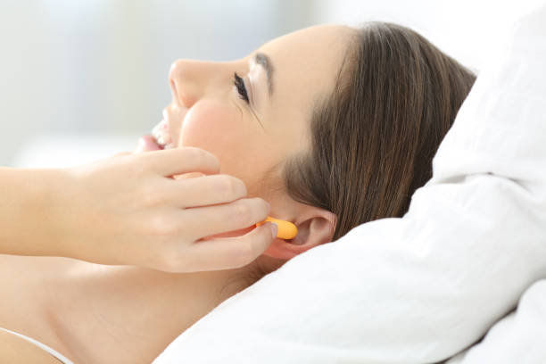 Woman covering ears using plugs on the bed Side view of a woman hand covering ears using plugs on the bed ear plug stock pictures, royalty-free photos & images