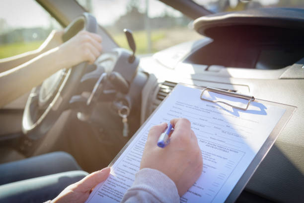 Examiner filling in driver's license road test form Examiner filling in driver's license road test form sitting with her student inside a car drivers license photos stock pictures, royalty-free photos & images