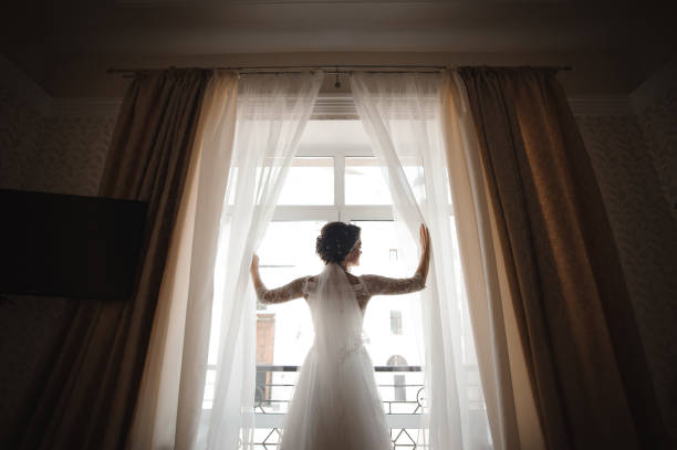 istock beautiful bride in a white wedding dress opens the curtains 944130042