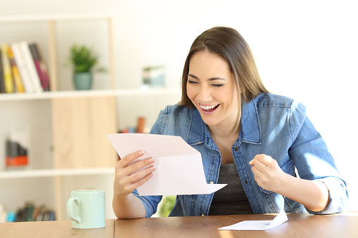 Portrait of an excited woman reading good news in a letter at home